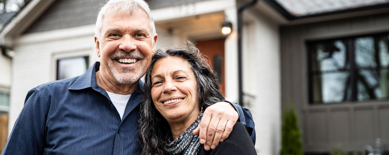 Older couple smiling together in front of their home