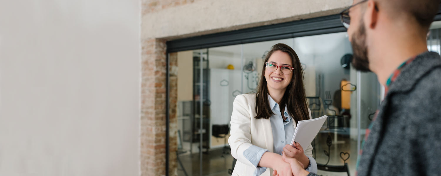 Woman holding paperwork and shaking a man's hand